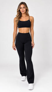 Calça flare preta cintura alta feminina com cós largo, vista de frente com top preto e tênis branco