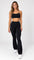 Calça flare preta cintura alta feminina com cós largo, vista de frente com top preto e tênis branco